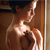 A pixelated figure with light skin tone stands in a doorway, holding a dark object near their chest, with a wooden door frame visible on the right side.