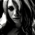 Black-and-white pixelated image of a person with light-colored hair, dark eye makeup, and a neutral expression against a solid black background.