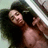 A shirtless person with long dark hair lies on a light green surface, making a peace sign with their right hand while holding a phone to their ear.