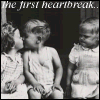 Black-and-white image of three children with text 'The first heartbreak.' at the top, showing a girl kissing a boy's cheek while another child looks on.