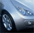 Pixelated image of a dark vehicle wheel and part of a light-colored car body against a blue sky background.