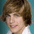 Pixelated portrait of a person with brown hair and light skin, wearing a white shirt against a teal background.