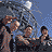 Animated contact sheet of Beastie Boys promotional icon frames showing band members, text overlays, and changing poses against a blue sky background with tree branches.