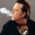 Pixelated static image of a person exhaling smoke with a small dog or animal on their shoulder, wearing dark clothing against a gray background.