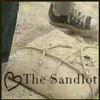 A static image shows a close-up of a light-colored fabric surface with a dark blue fabric edge, a shoe with visible text, and overlaid text reading 'The Sandlot' with a heart symbol.