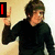 A person in a black long-sleeve shirt makes a peace sign with their right hand against a light-colored wall background.