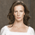 Pixelated portrait of a person with long brown hair wearing a white top against a gray background.