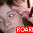 A pixelated close-up of a person with light skin and dark hair, wearing a red rectangular graphic with white text.