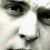 A pixelated close-up of a face with dark hair and eyes, showing partial features against a light background.