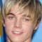 Static close-up of a person with light brown hair and blue eyes against a gradient background.