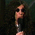 Pixelated static image of a stylized human figure with dark hair and sunglasses holding an object against a dark background.