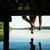 Pixelated static image shows a figure hanging upside down from a tree branch above water with two dark posts in the foreground.