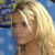 A static pixelated image shows a person with long blonde hair against a blue background with blurred green and purple elements.