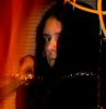 A person with long dark hair and a black top appears in front of an orange curtain, with blurred background elements including yellow lines.