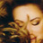 Pixelated close-up of a person's face with closed eyes and flowing hair, rendered in warm brown and orange tones on a dark background.