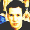 A static image of a person with dark hair wearing a black top, with a blue and white patterned background element visible on the left side.