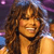A pixelated static image shows a person with long curly brown hair, wearing a dark top against a blurred background with purple and blue tones.