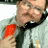 A pixelated close-up of a person wearing a light-colored shirt and dark tie with a red emblem on the chest, cropped to show only the upper torso and face.