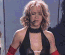 Britney Spears in three distinct poses: black halter dress with red arm bands, red gown holding a microphone, and dark sleeveless dress on stage with fire effects.