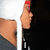 A person with red-painted fingernails holds a white object against their face, wearing a gray top and white headband.