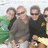 Four pixelated figures in casual clothing stand closely together against a blurred green and white background.