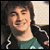 Static pixelated image of a person with long dark hair wearing a green shirt and black jacket, smiling against a light background.