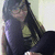 A person with long dark hair and glasses wears a sleeveless top, seated against a light background in a pixelated image.