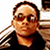 Pixelated static image of a person wearing sunglasses and dark clothing with visible dithering effects on the background.