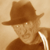 Pixelated static image of a character wearing a brown fedora and dark jacket against a beige background, with visible dithering and low-resolution rendering artifacts.