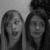 Two women in grayscale; left woman has mouth open, right woman has closed mouth; background is plain light gray.