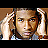 Pixelated static image of a person with light skin tone, dark hair tied back in a ponytail, wearing a white top and blue garment underneath, positioned against a brown background with visible pixelation artifacts.