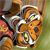 Two orange-furred animals with white markings on their faces and bodies are positioned closely together, one slightly behind the other, against a blurred background.