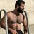 Pixelated image of a shirtless man with dark hair and beard standing against a light background holding a crutch.