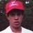 Pixelated static image of a person wearing a red cap and white shirt against dark background.