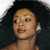 Pixelated close-up of a person with dark curly hair, light brown skin, and a small earring, set against a dark background with a light gradient on the left.