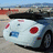 A pixelated image of a white convertible car with red taillights and a blue license plate, set against a beach background with distant buildings.
