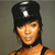 Pixelated image of a person wearing a black cap with a white emblem, dark hair, and an orange top against a gray background.