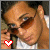 A 50x50 pixel animated buddy icon showing a person with dark hair and sunglasses in two sequential frames, each featuring a red heart symbol at the bottom left.