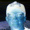 Two side-by-side pixelated portraits: left shows a blue-tinted figure with white hair against black background, right shows a person with dark cap and glasses against light background.