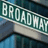 Green street sign reading 'BROADWAY' on left, white text 'SARAH' on black background on right, both in pixelated style.