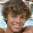 Pixelated close-up of a person with curly brown hair, light skin, and a smiling expression against a blurred background.