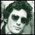 Pixelated grayscale portrait of a person with curly hair and dark sunglasses, displayed as a static buddy icon.