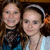 Two women in a group photo, one wearing a white headband and light blue top, the other with long brown hair and dark clothing.
