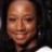 A pixelated close-up of a person's face with light skin tone, dark hair visible on the right side, and neutral expression against a dark background.