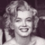 Pixelated grayscale image of a smiling person with curly hair, wearing a light-colored top against a dark background.