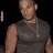 Pixelated static image of a person in dark clothing with visible tattoos on the arm and chest, wearing a necklace against a black background.
