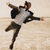 A person in a gray shirt and dark pants performs a dynamic jump with arms outstretched against a light background.
