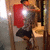 A person in a silver helmet and red shield stands in a bathroom holding a camera, with a toilet visible behind them.