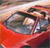 A pixelated image of a red vehicle with a visible headlight and windshield, set against a blurred background with warm tones.