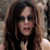 A pixelated close-up of a person with long dark hair wearing dark sunglasses and a dark top against a blurred background.